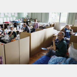 束の間のしのぎに段ボールの間仕切りがされ避難所で、配られた氷アイスで酷暑をやり過ごす人びと＝8月3日（Ｃ）共同通信社